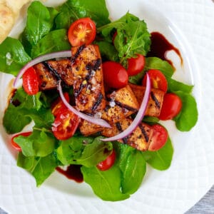 Arugula salad with savory pepper grilled tofu medallions and balsamic glaze.