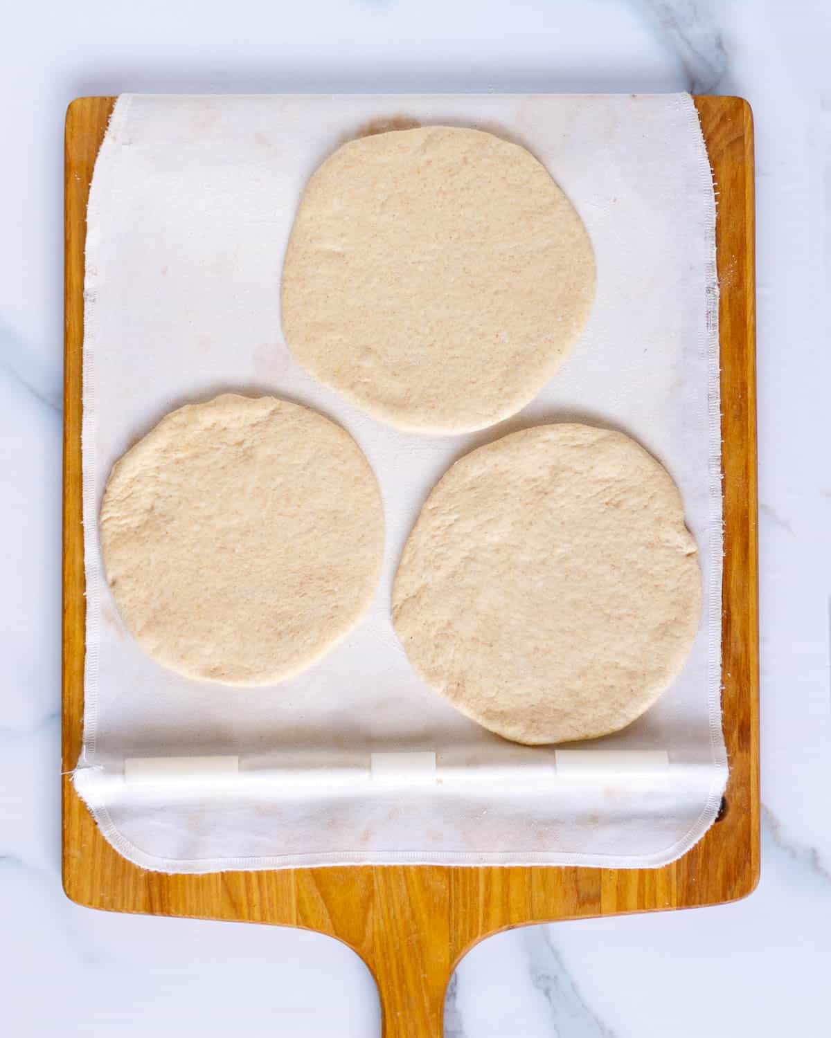 Three flat pieces of bread dough on a baking peel.