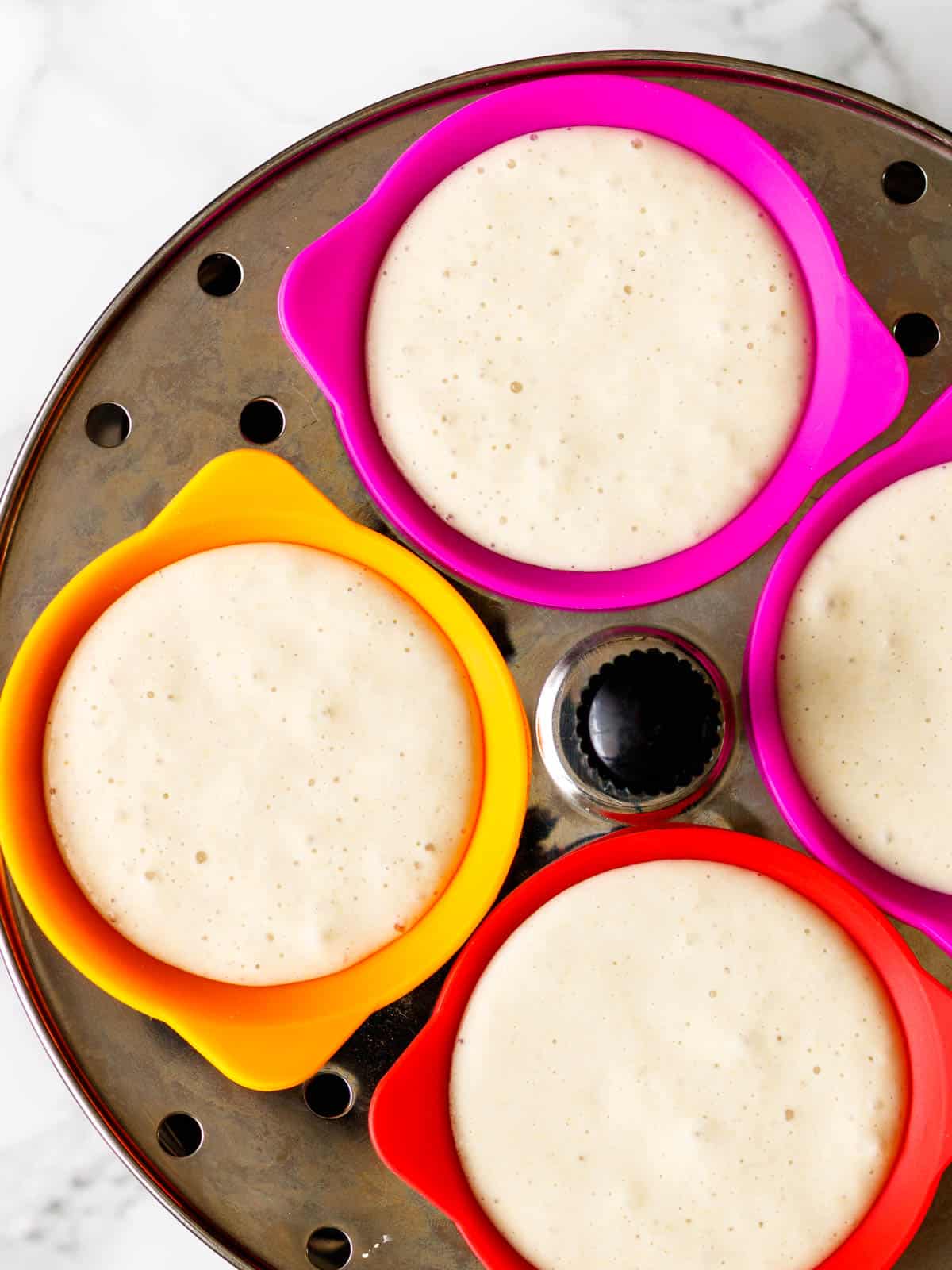Idli batter in liners on steaming tray.