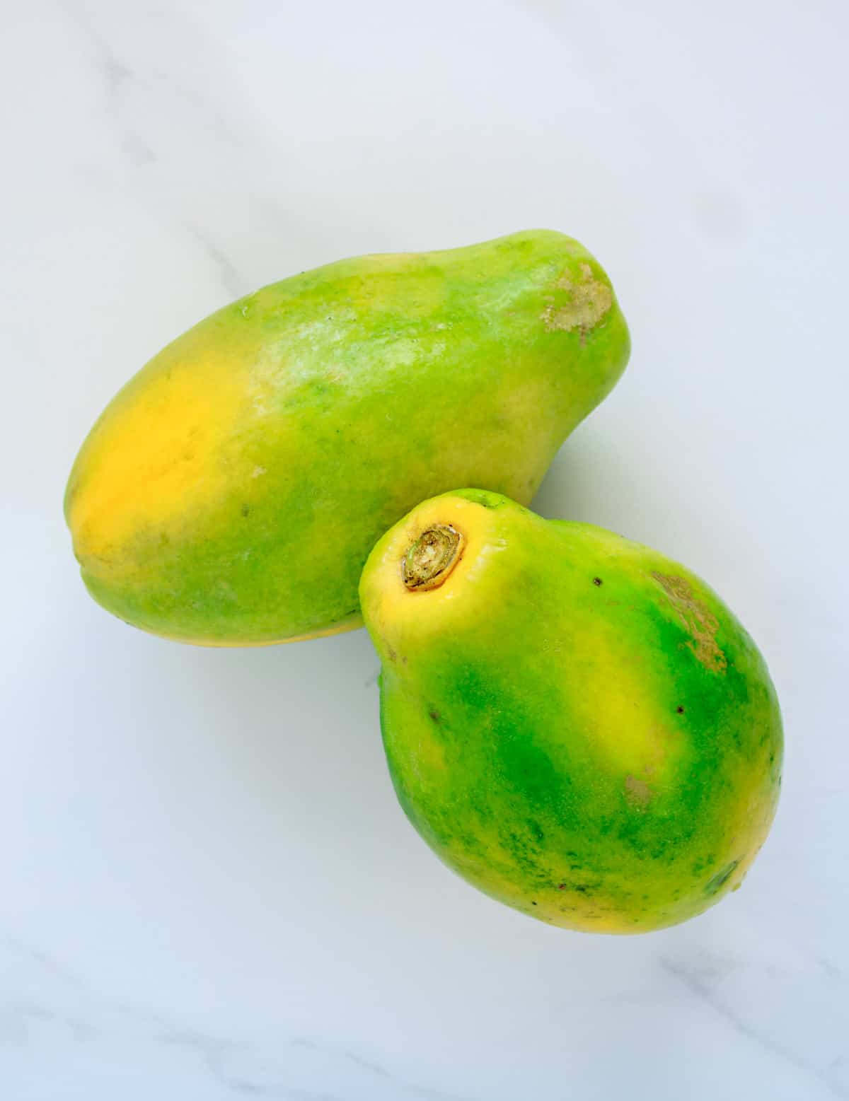 Two whole papayas half yellow and half green in color.