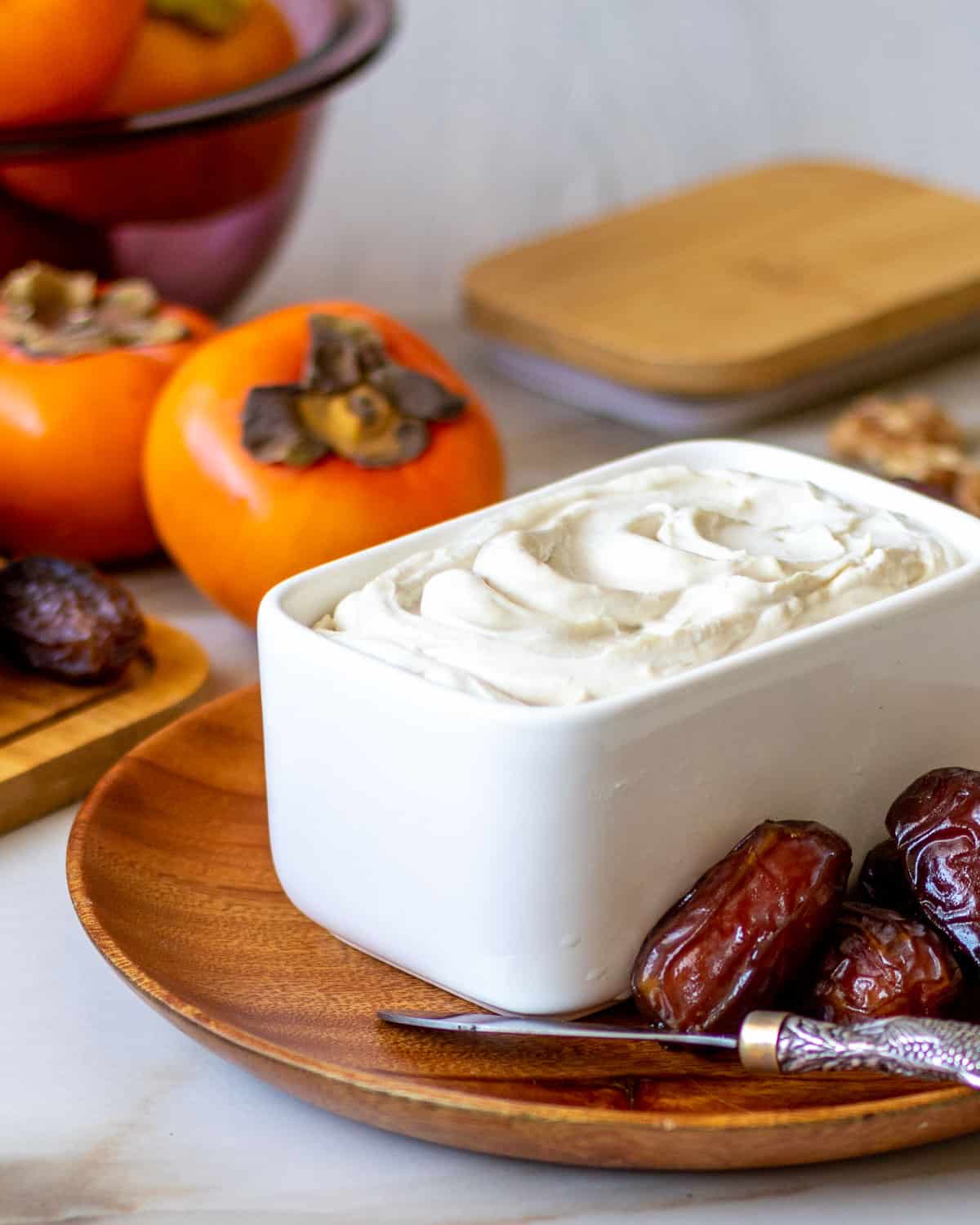 Ceramic pot with homemade vegan cream cheese surrounded by fruit.