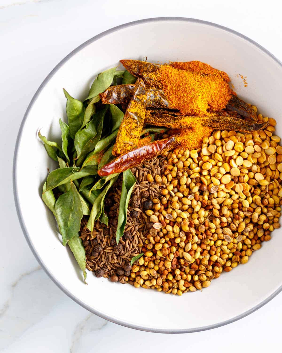 Bowl of toasted Indian spices with chilis and curry leaves.