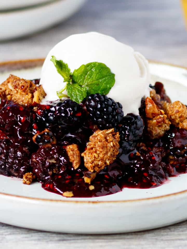 Plate of blackberry crumble with ice cream melting over the top.