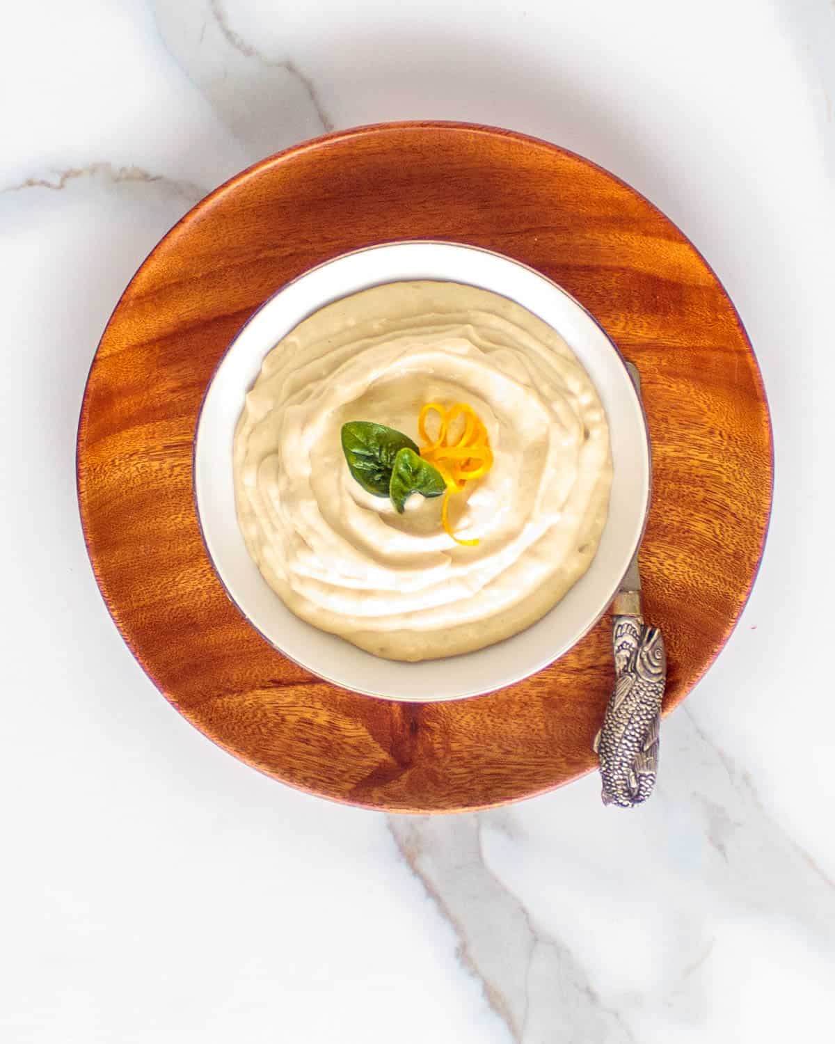 Bowl of thick vegan tahini sauce garnished with oregano and lemon zest.