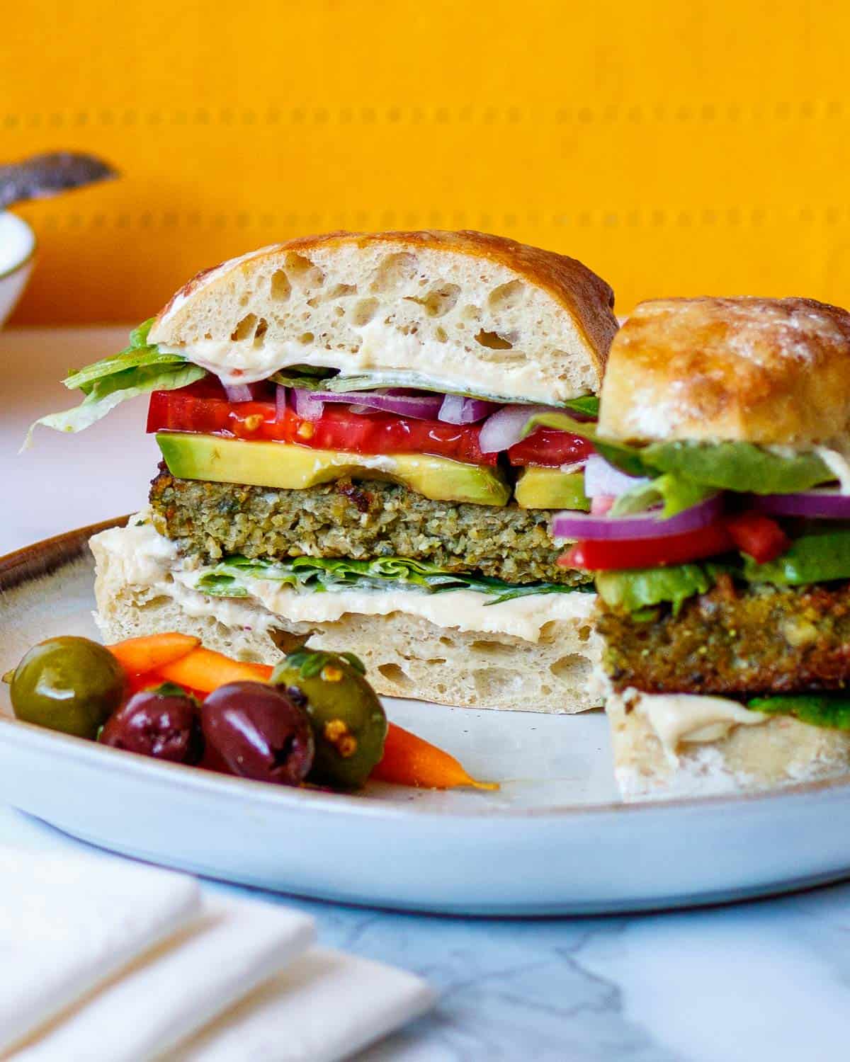Falafel sandwich on a plate with carrots and olives.