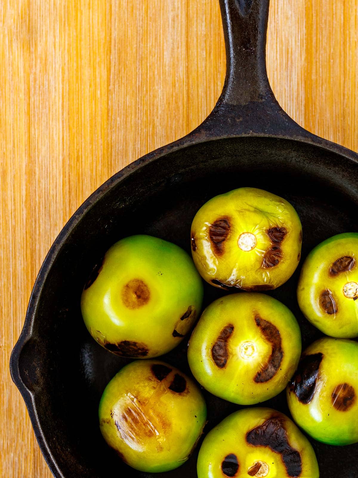 Charred whole tomatillos in cast iron skillet.