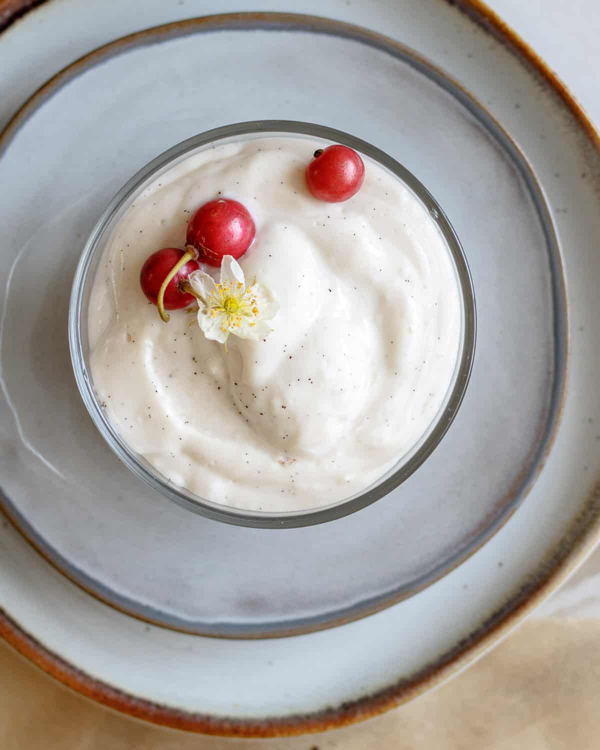 Bowl of creamy vegan vanilla pudding decorated with three berries and a flower.