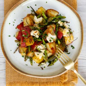 Plate with roasted red and yellow potatoes, baked with asparagus and topped with goat cheese.