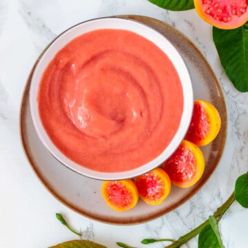 Bowl of homemade guava puree surrounded by fruit.