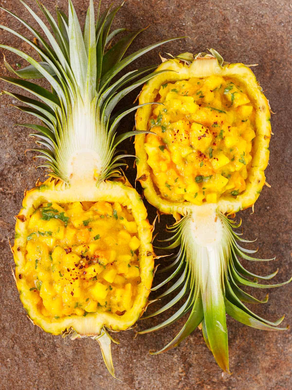 Two halved pineapple shells filled to brim with spicy fruit salsa.