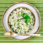Bowl of fluffy green rice pulao on a colorful mat.