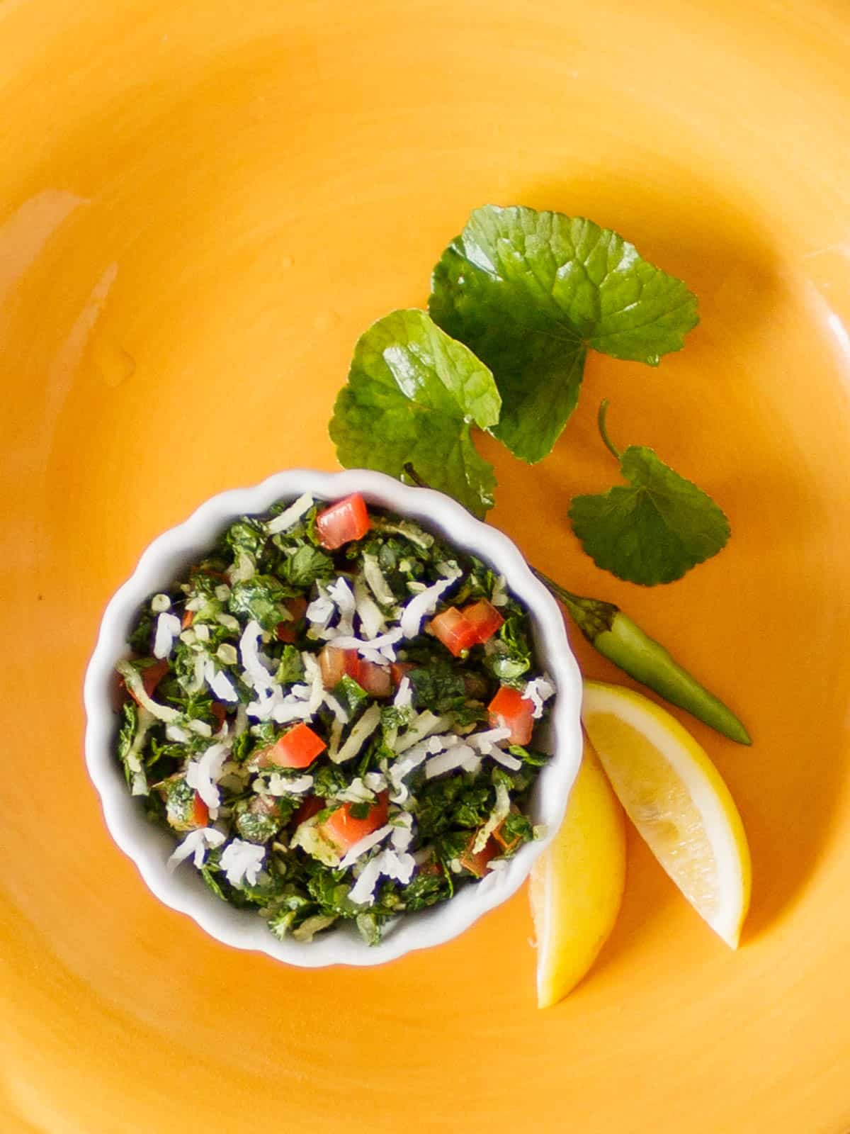 Small bowl of Indian pennywort salad with lemon and green chili on the side.