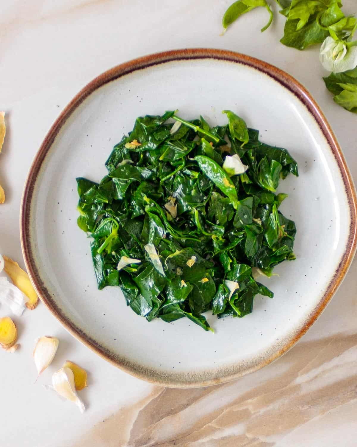 Plate with bright greens cooked snow pea leaves with ginger and garlic.