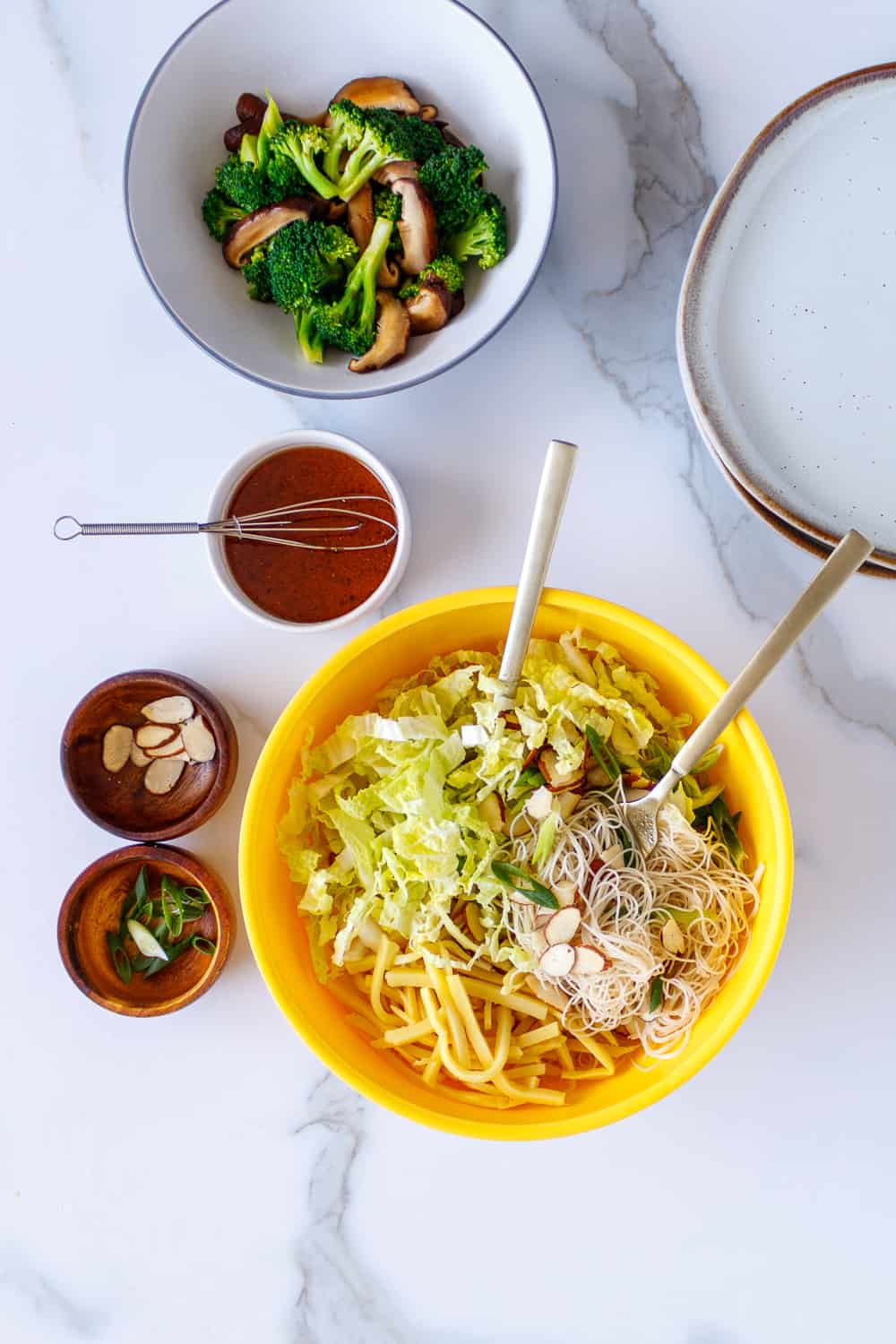 Yellow bowl with tossed mei fun noodles and cabbage with separate bowls of vegetable toppings.