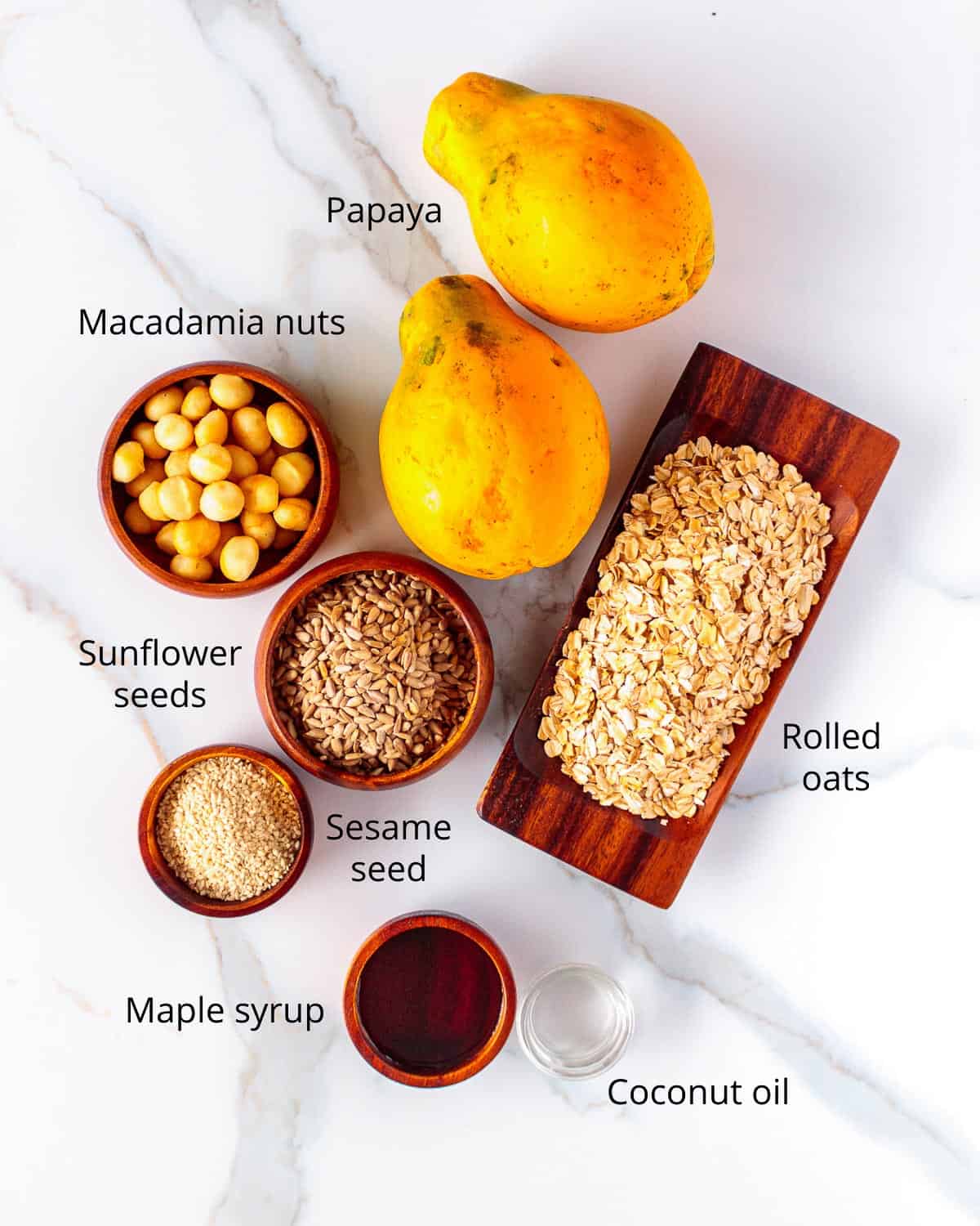 Whole papaya, macadamia, sunflower seed, sesame seed, oats, maple syrup and coconut oil in dishes.