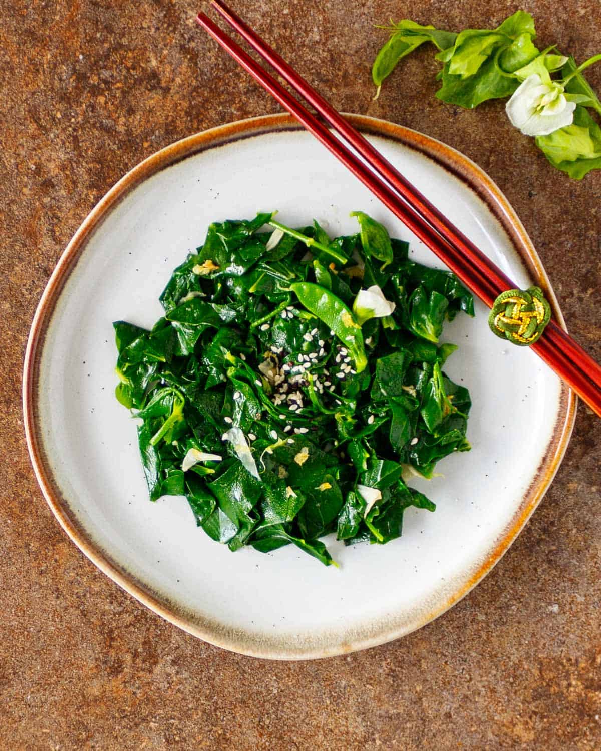 Plate of dark green stir-fried leaves with sesame seeds on top.