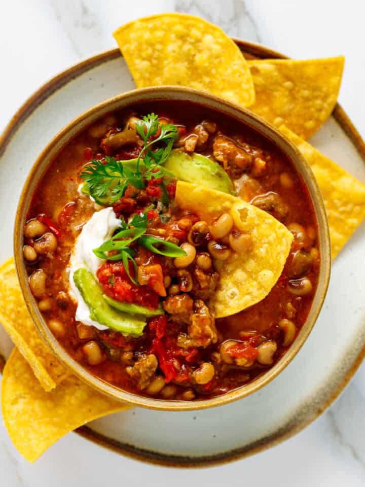 Bowl of black eyed pea chili with toppings and corn chips.