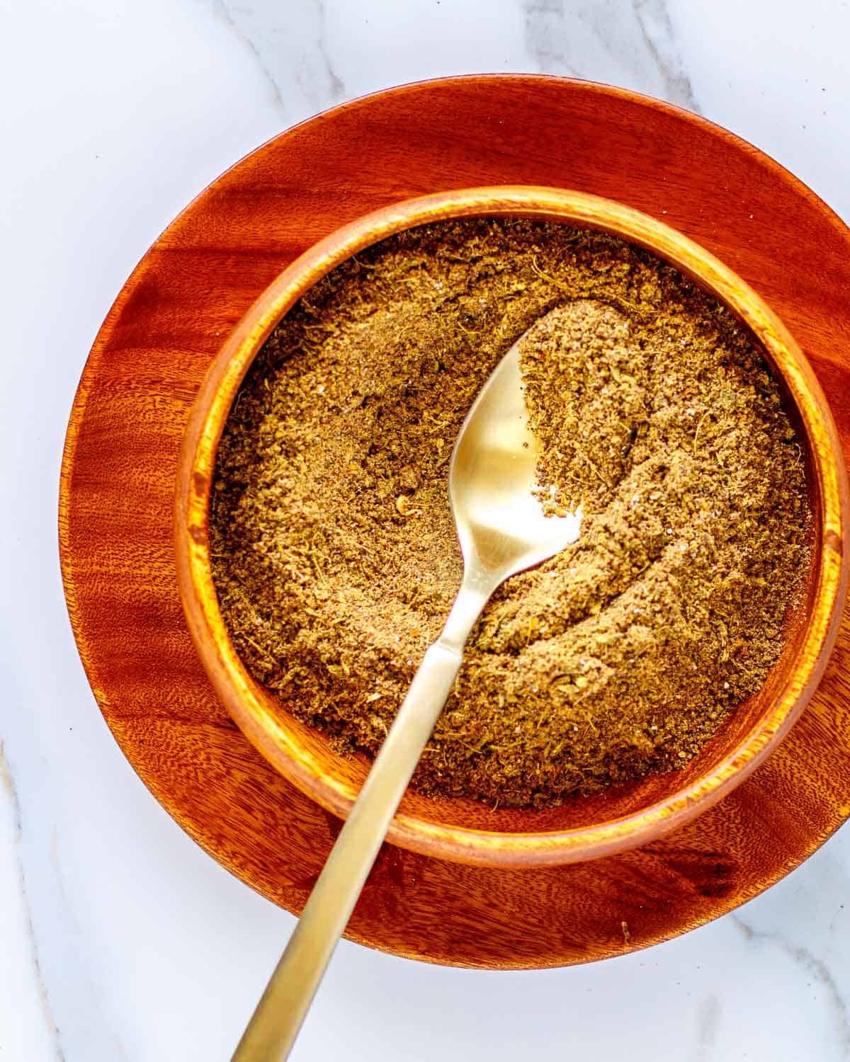 Powdered spices in a wooden bowl with a gold spoon.
