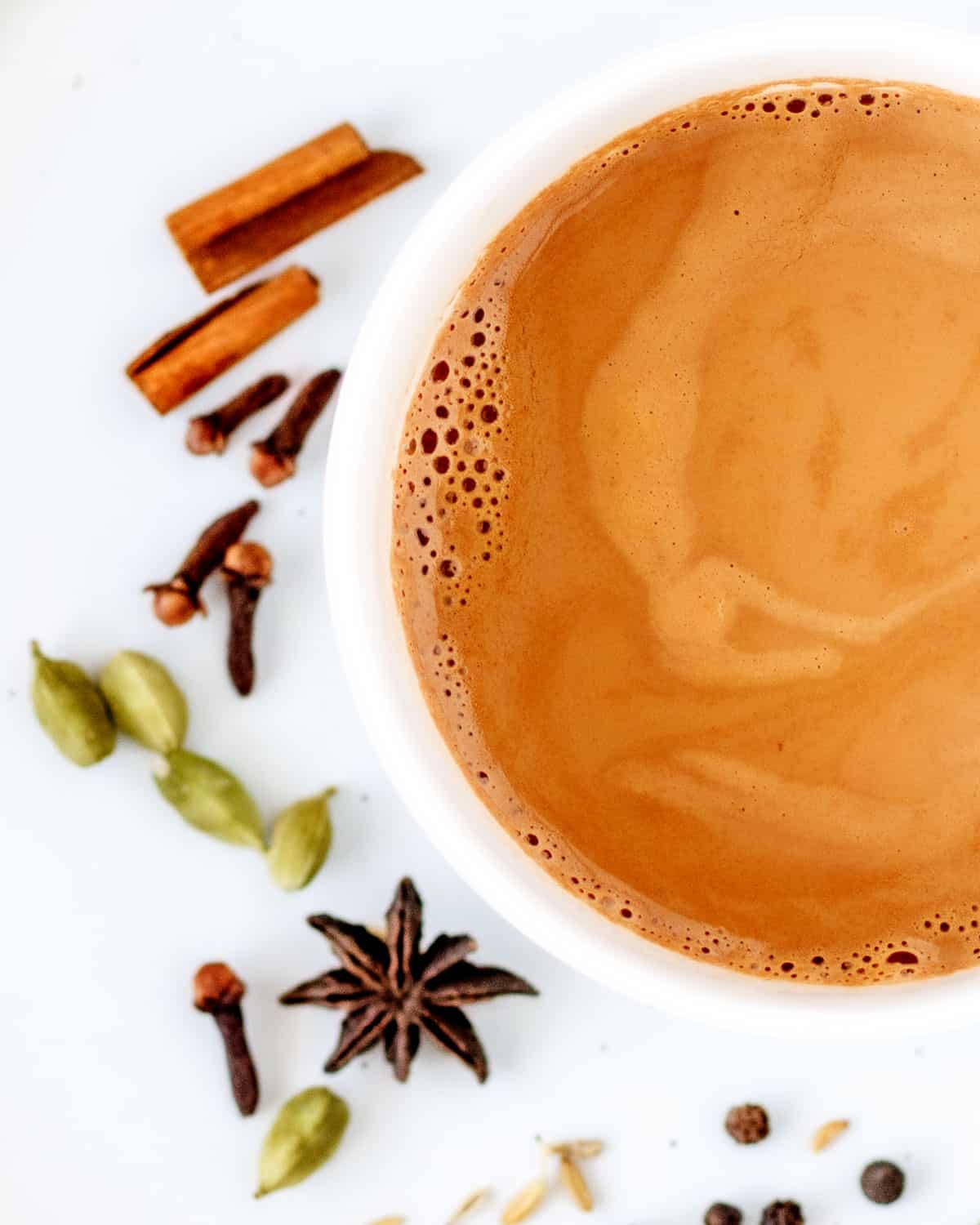 Cup of masala chai with spices on tile.