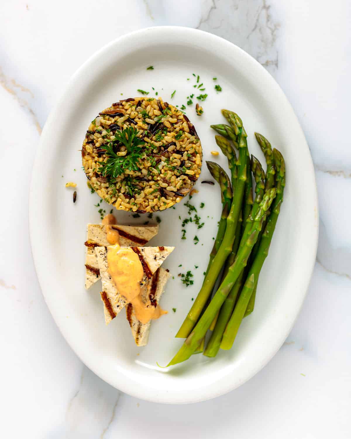 Oval plate wilth wild rice pilaf, asparagus and tofu.