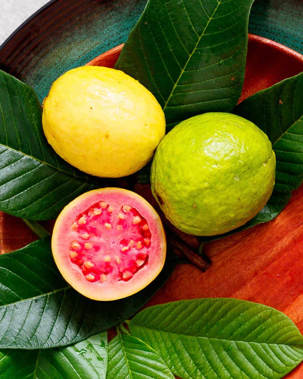 Guavas, yellow, green and cut in half showing pink pulp and seeds.