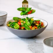 Bowl of sauteed snow peas with a fork piercing three peas.