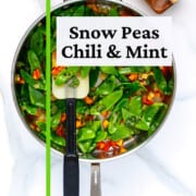 Snow peas in a skillet cooked with chili flakes and mint.